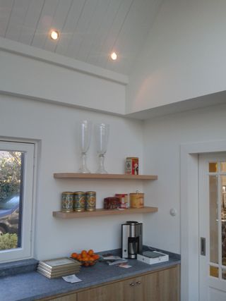 Keukenwand met inbouwspots in het schuine plafond, wandplanken en een aanrecht