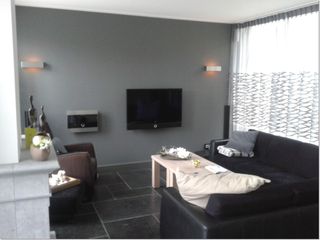 Woonkamer met wandverlichting, een televisie aan de muur en een hoekbank